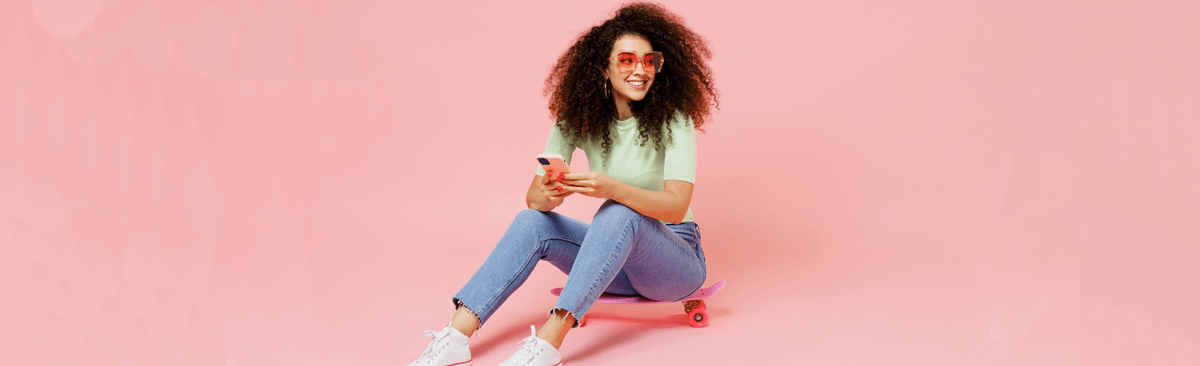 Happy woman sitting on skateboard, using phone