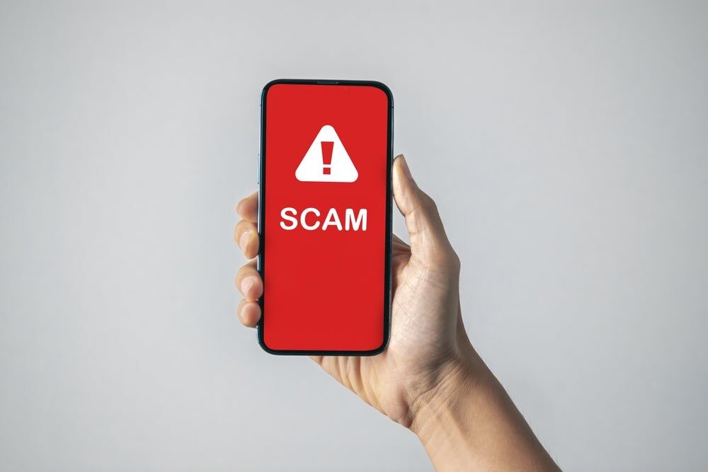 Photo of phone with the text scam and a warning symbol