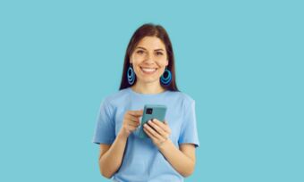 Woman smiling while holding her phone in front of a blue background.