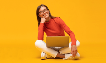 Young woman using laptop against orange background.